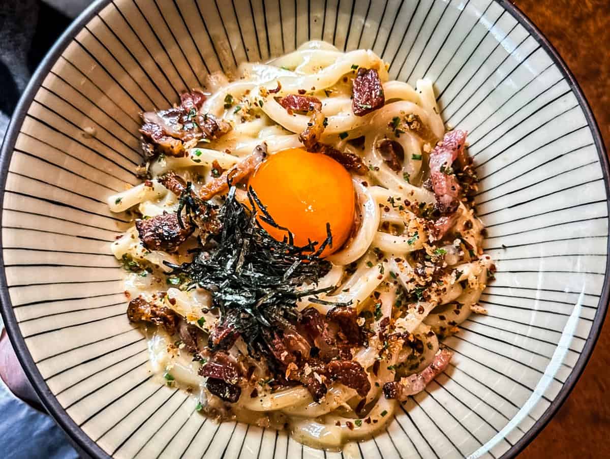 A plate with noodles, guanciale, seaweed and a yolk in the middle.