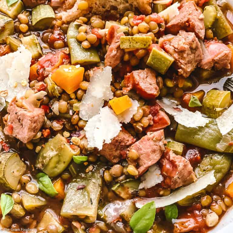 Close up of a lentil sausage soup with veggies and parmesan cheese and a piece of bread.