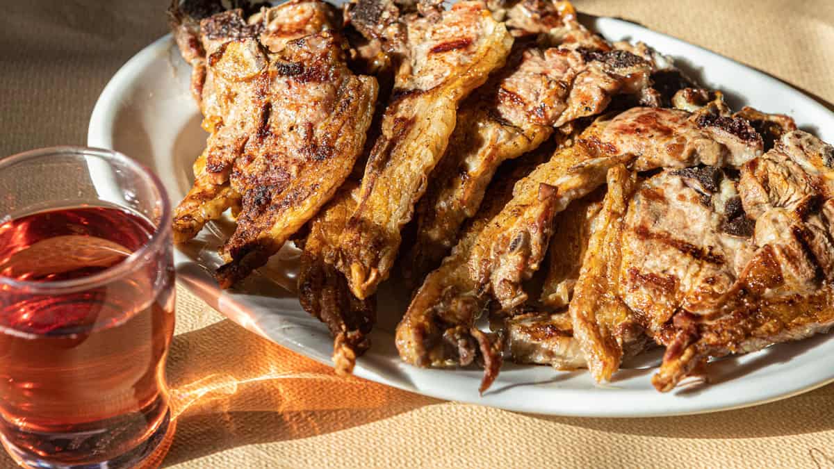 Paidakia-Greek lamb chops on a plate, next to a glass of wine.