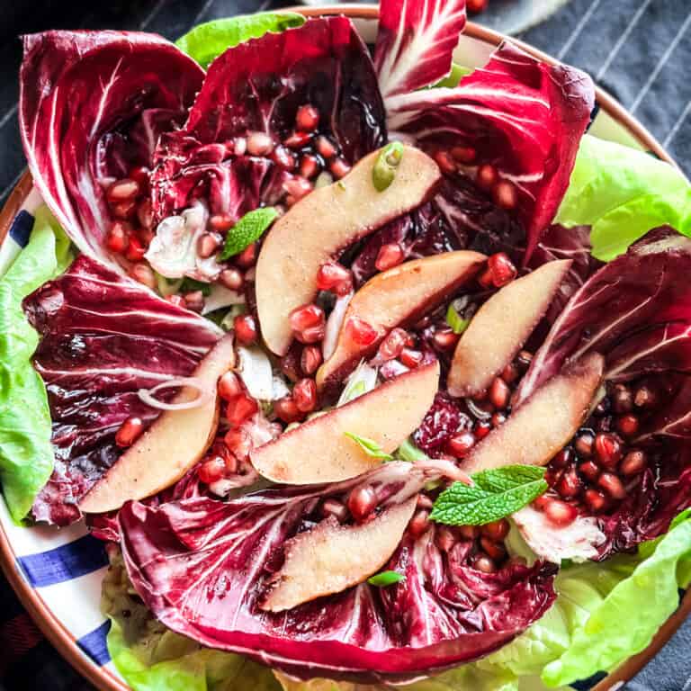 A pomegranate salad with roasted sliced quince radicchio and lettuce on a platter.