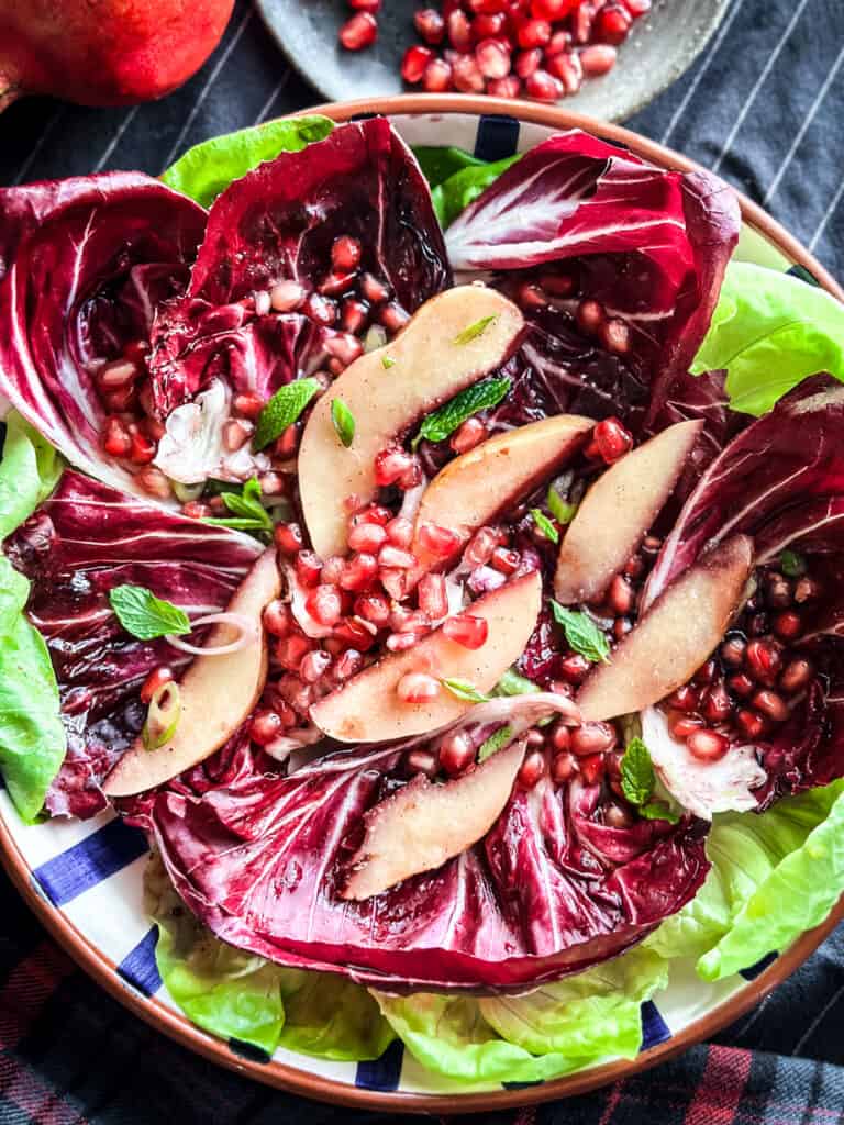 A pomegranate salad with roasted sliced quince radicchio and lettuce on a platter.