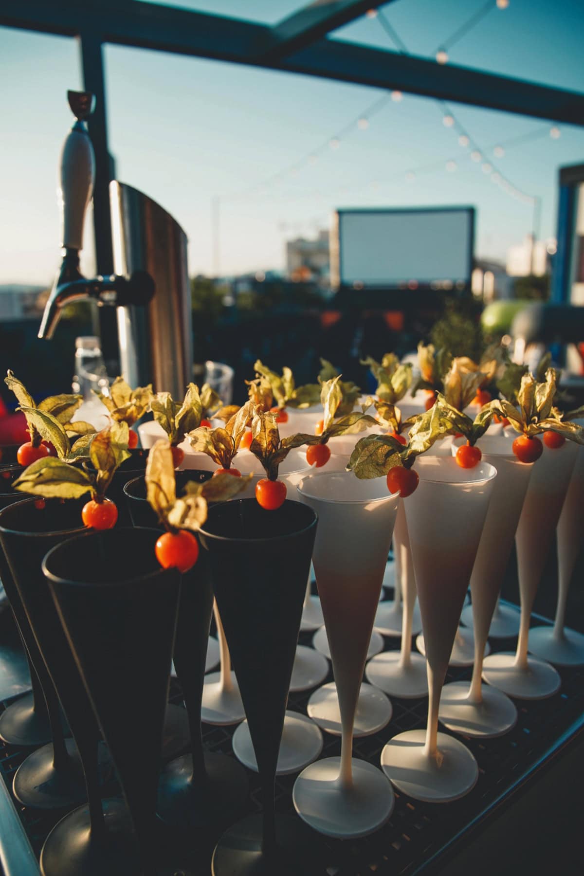 Champagne glasses, lined up with a cherry on the rim, at the back an outdoor cinema.