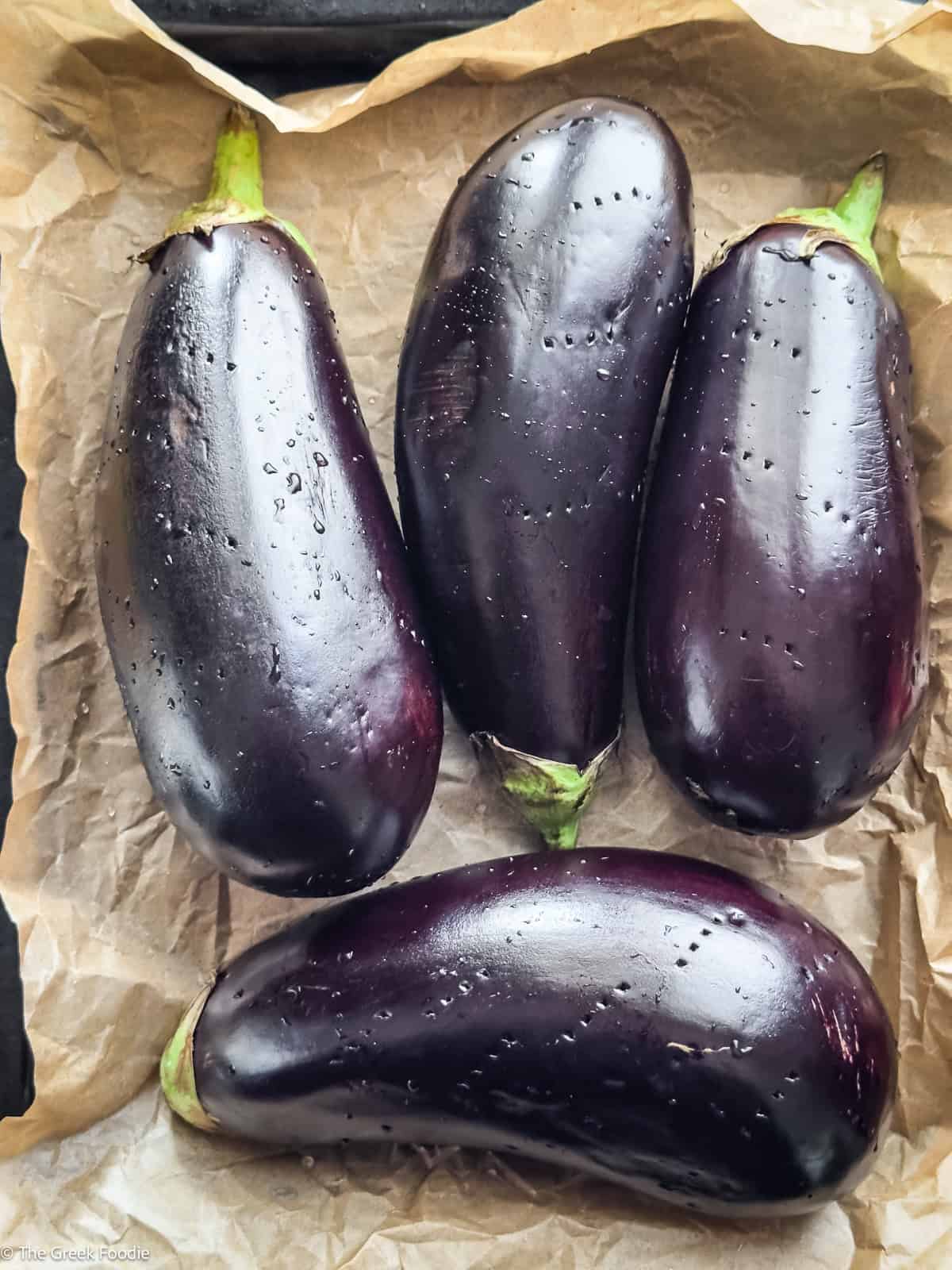 Four eggplants on a tray, with fork marks on them.