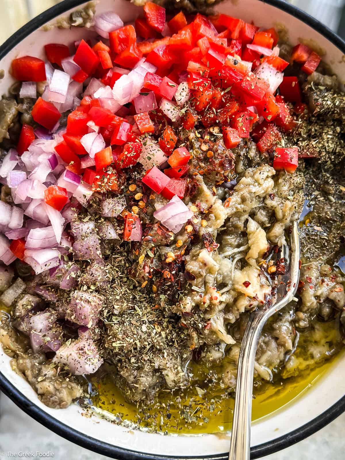 Roasted eggplant pulp mixed with chopped red pepper, onion, olive oil, oregano, and chili flakes for Greek melitzanosalata.