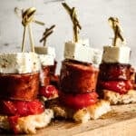 Greek sausage bites with tomato confit, feta cheese, and crusty bread served on wooden board