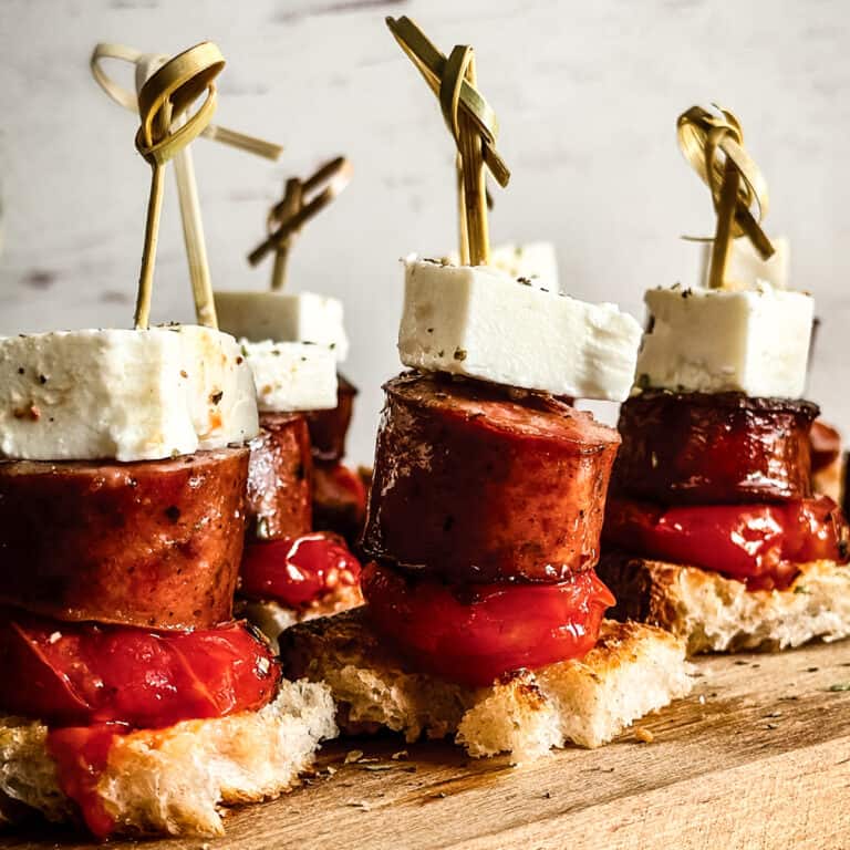 Greek sausage bites with tomato confit, feta cheese, and crusty bread served on wooden board