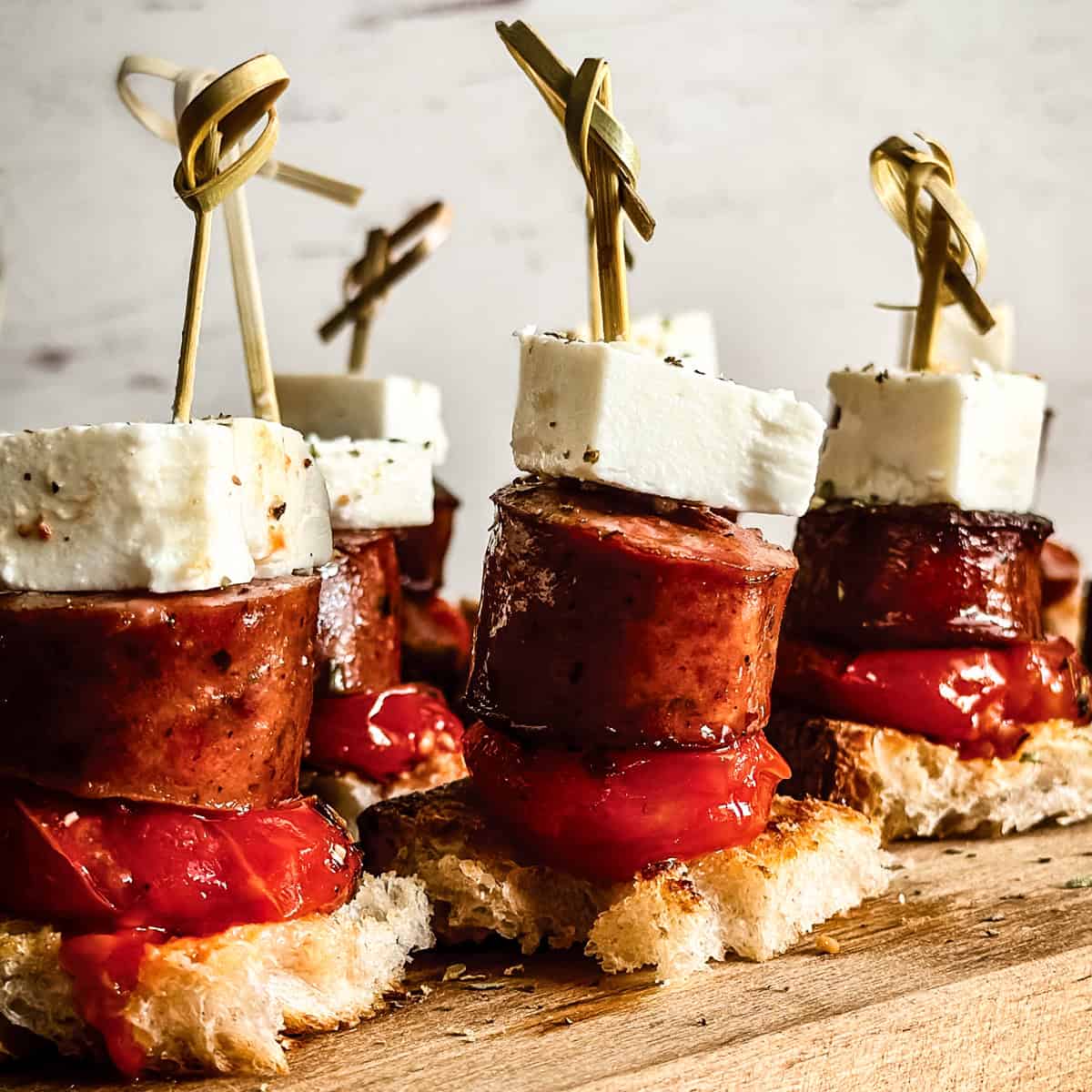 Greek sausage bites with tomato confit, feta cheese, and crusty bread served on wooden board