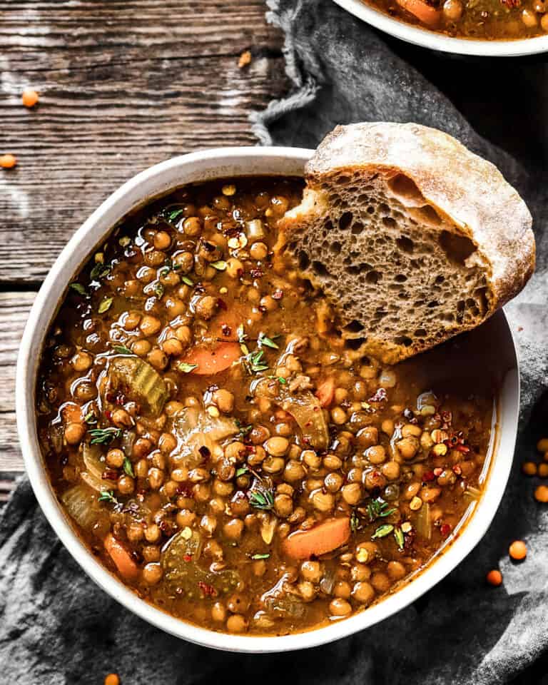 A bowl of Greek lentil soup with a piece of bread on a table.