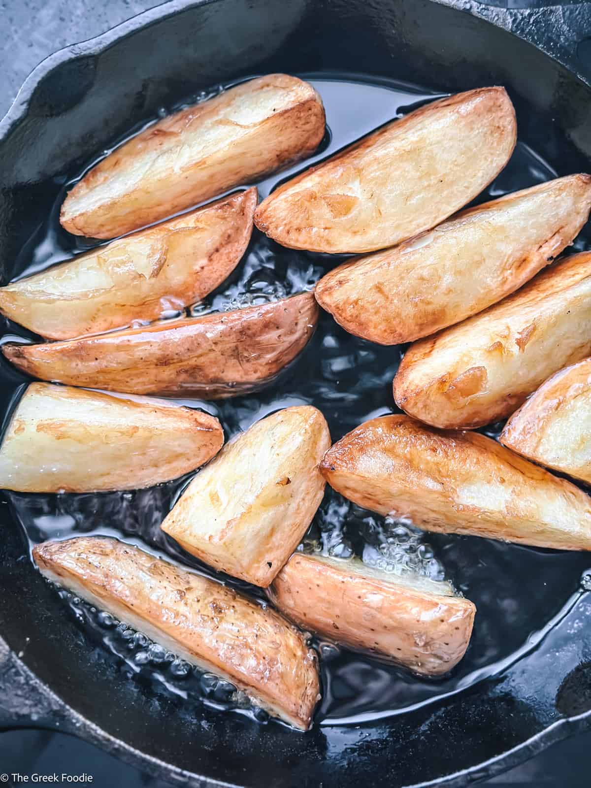 Golden fried potato wedges cooking in olive oil until crisp on the outside and fluffy inside.