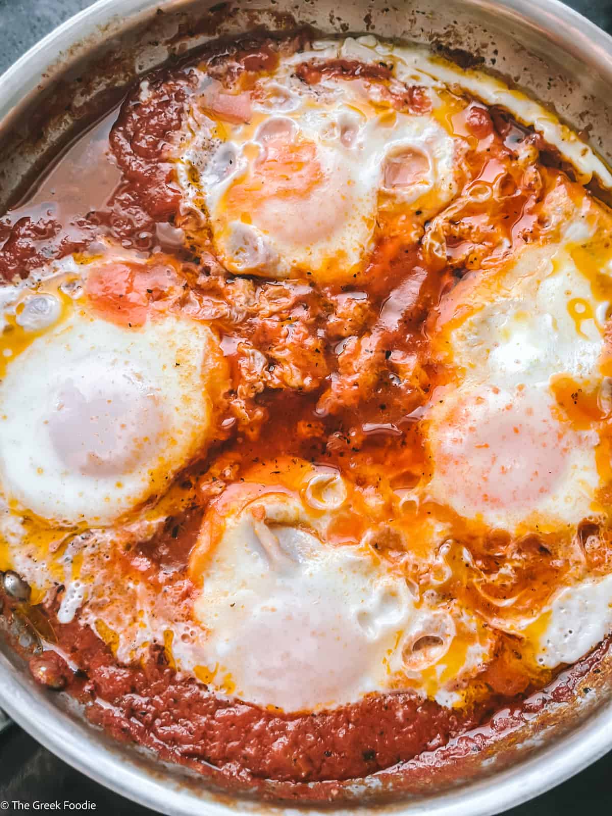 Eggs gently cooking in spiced tomato sauce with set whites and soft yolks in a skillet.
