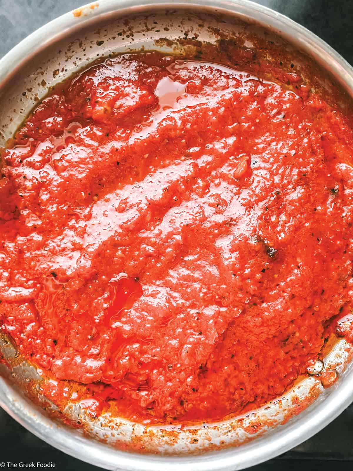 Grated tomatoes simmering in olive oil infused with spices, forming a rich Greek tomato sauce.