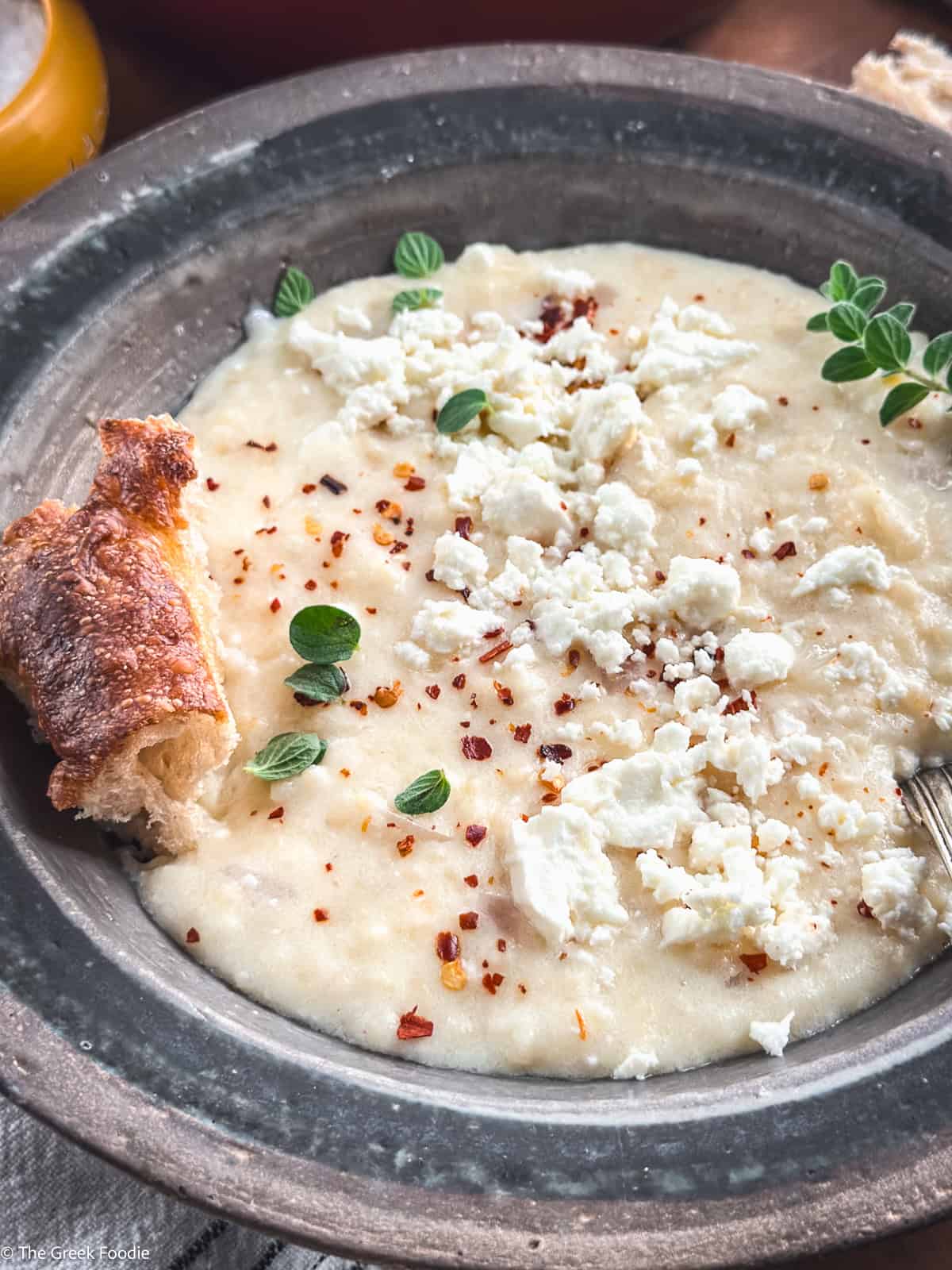 Creamy traditional Greek trahanas soup made with butter and feta, topped with cracked black pepper and chili flakes, served with crusty bread.