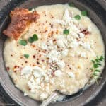 Creamy traditional Greek trahanas soup made with butter and feta, topped with cracked black pepper and chili flakes, served with crusty bread.