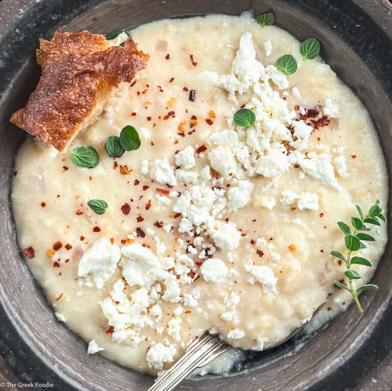 Creamy traditional Greek trahanas soup made with butter and feta, topped with cracked black pepper and chili flakes, served with crusty bread.