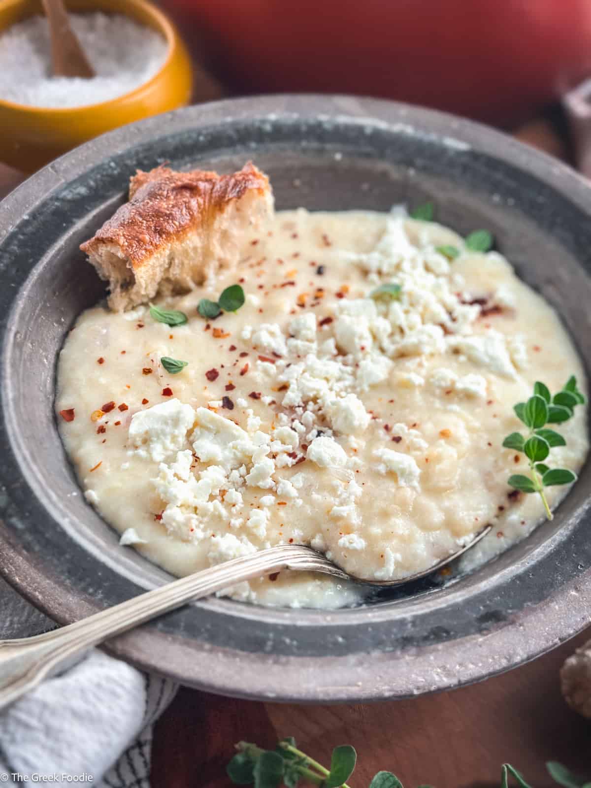 Creamy traditional Greek trahanas soup made with butter and feta, topped with cracked black pepper and chili flakes, served with crusty bread.