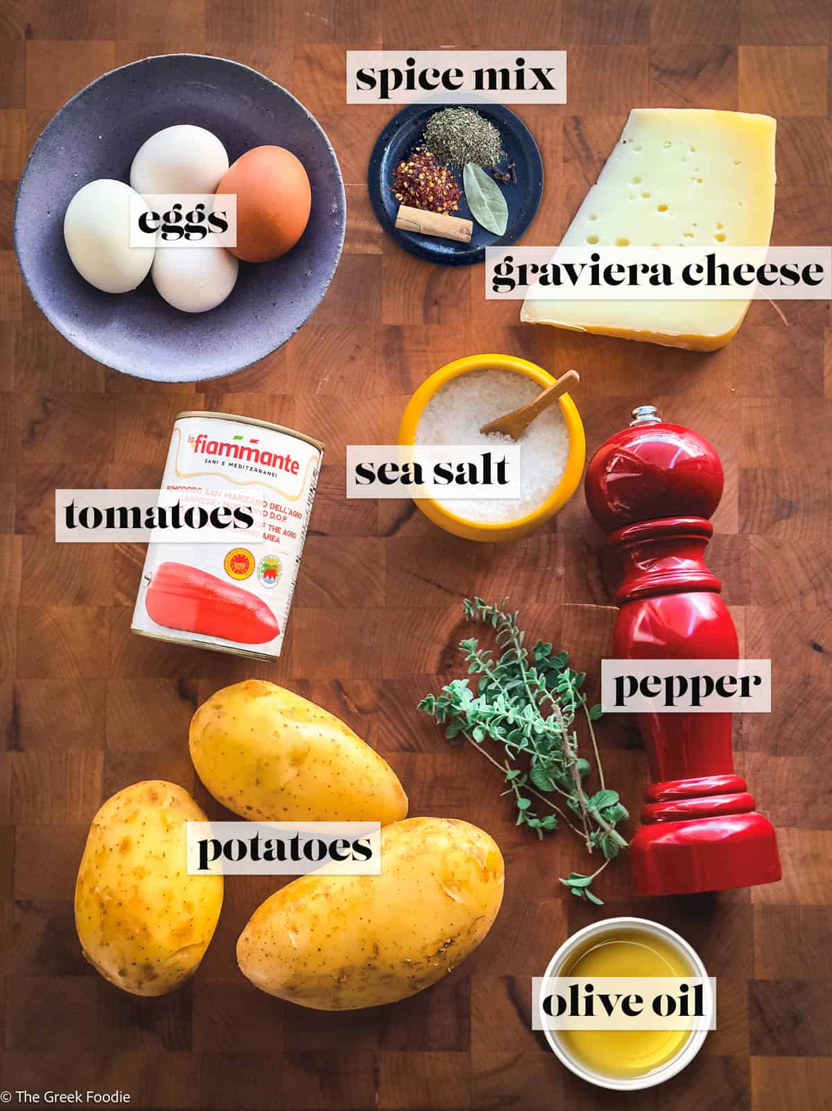 Ingredients for Greek eggs in tomato sauce, including eggs, potatoes, feta or graviera cheese, tomatoes, olive oil, salt, pepper, and fresh oregano.
