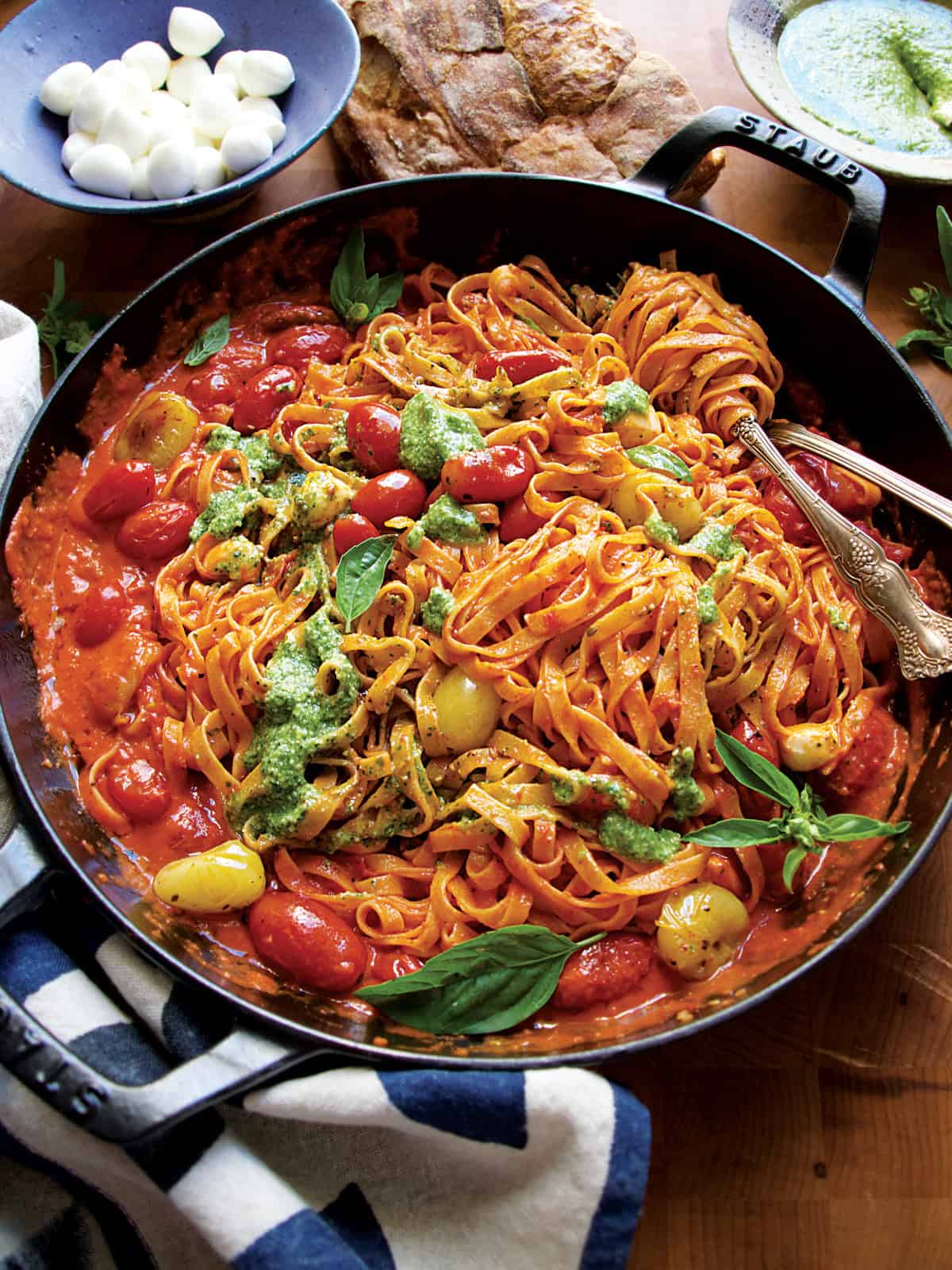 A cherry tomato pasta with pesto in a pan with herbs.