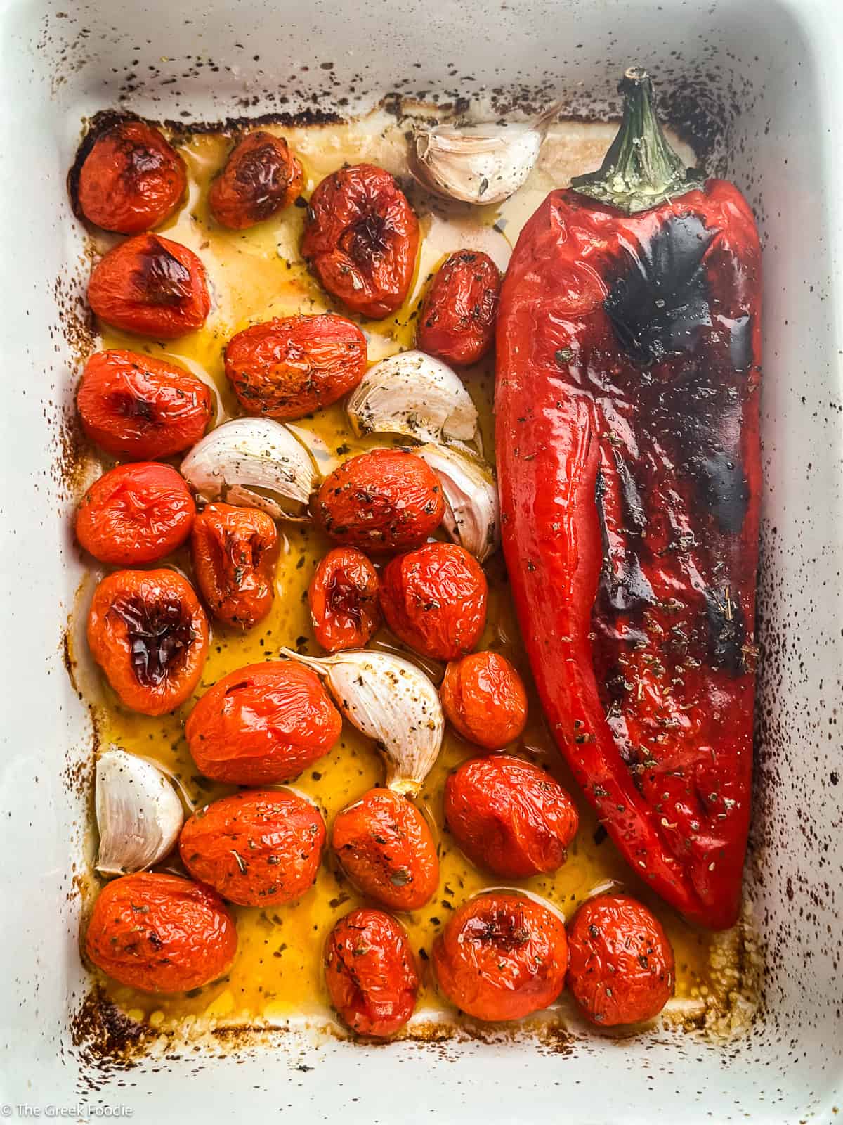 Charred cherry tomatoes, sweet roasted garlic cloves, and roasted red pepper on a baking dish.