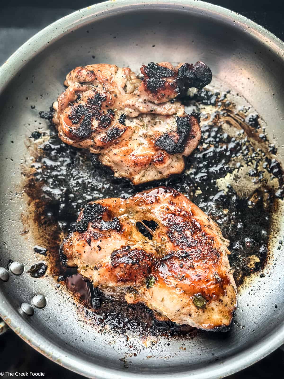 Greek chicken thighs searing in a skillet with caramelized edges and char from honey marinade