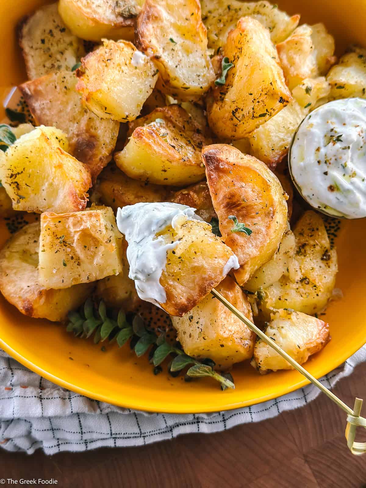 Roasted potato bite skewered and dipped into creamy tzatziki sauce, showing the fluffy interior and crisp exterior.