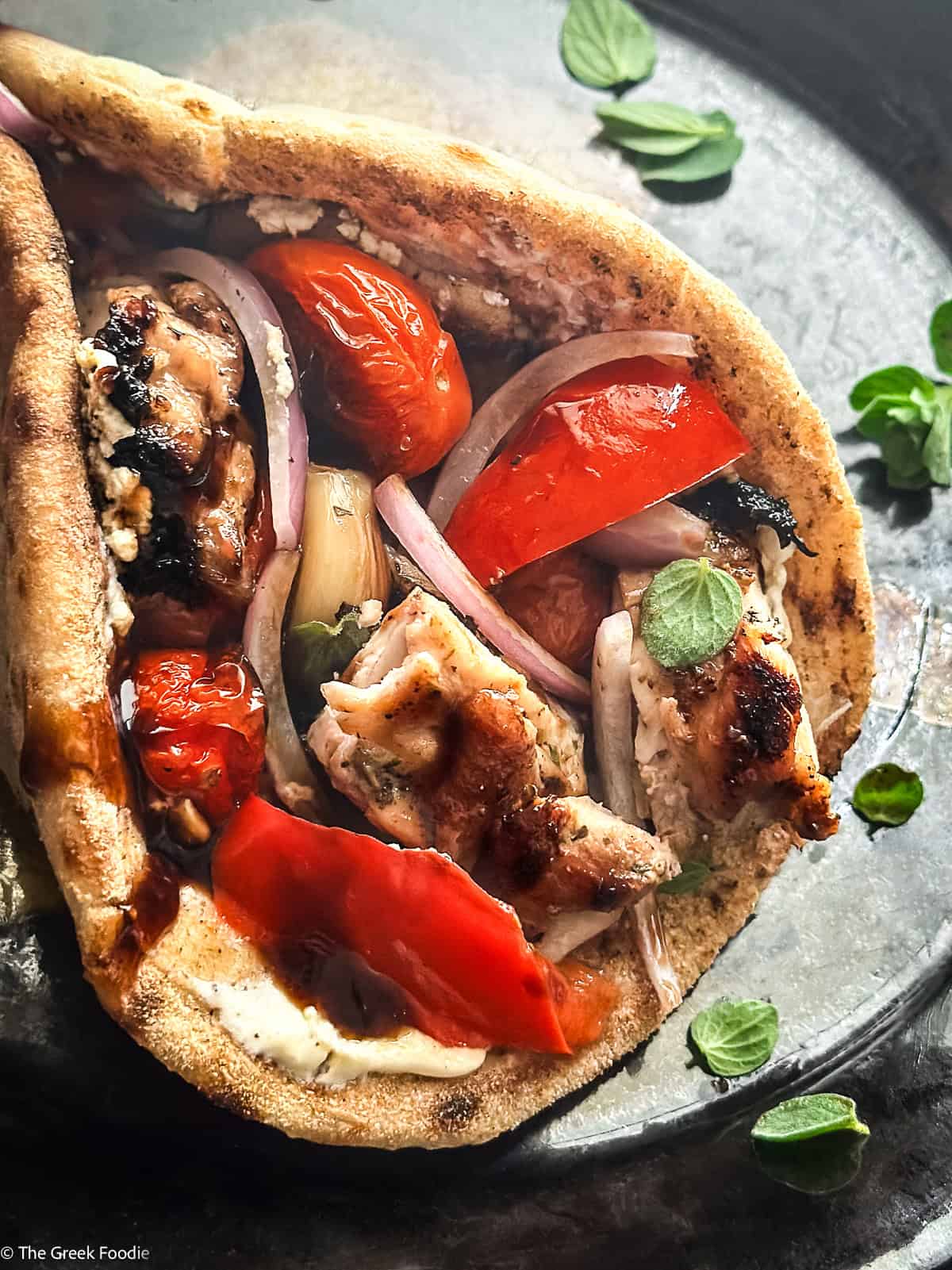 Folded Greek chicken pita wrap with roasted garlic, blistered tomatoes, and creamy yogurt-feta spread.