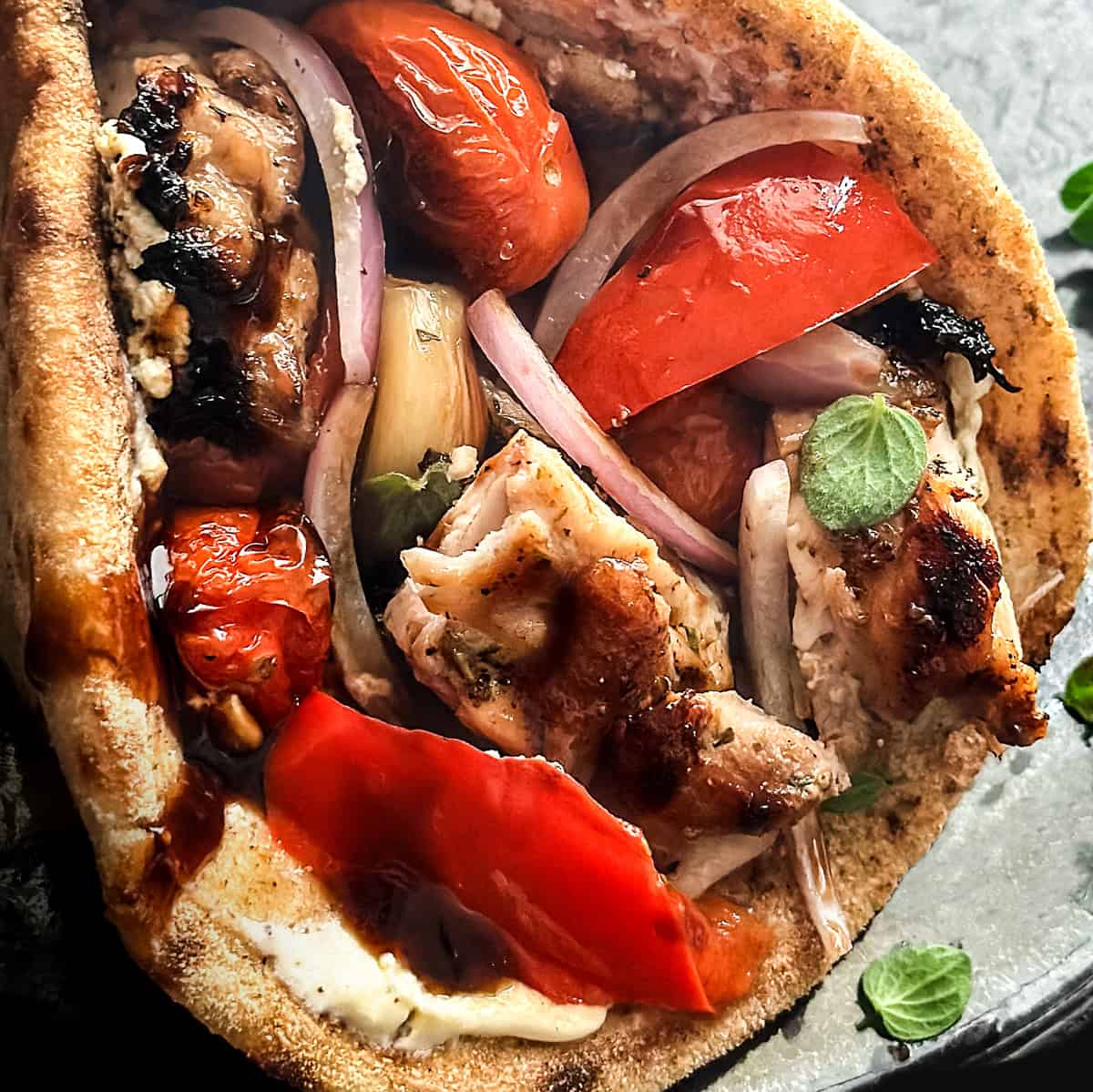 Folded Greek chicken pita wrap with roasted garlic, blistered tomatoes, and creamy yogurt-feta spread.