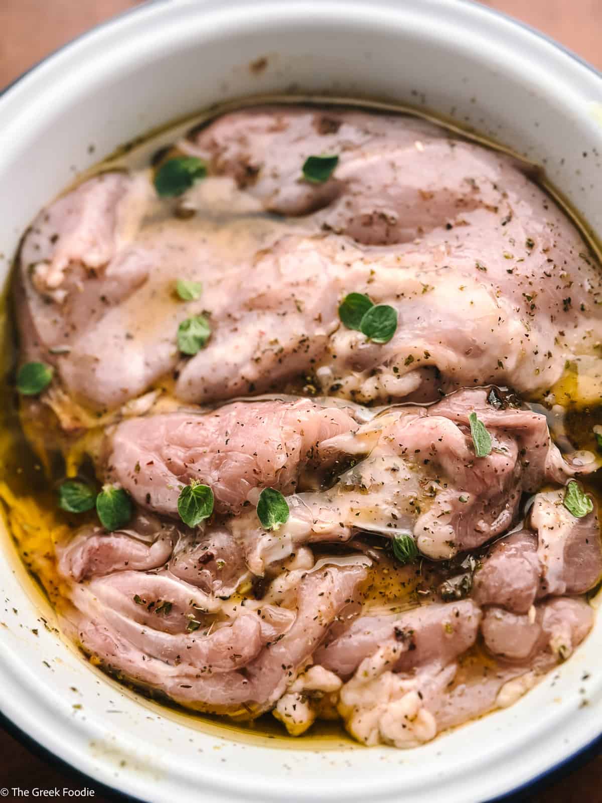 Boneless skinless chicken thighs marinating in olive oil, herbs, and honey before cooking.