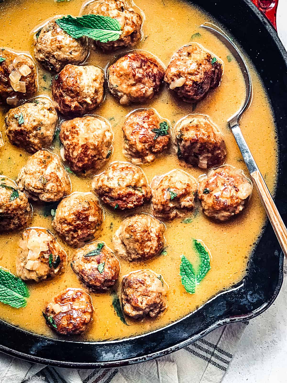 Turkey meatballs and gravy in a skillet with a spoon.