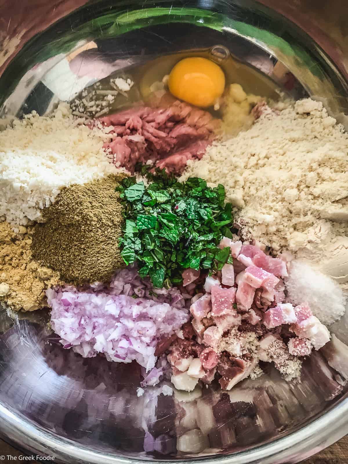 Ground turkey meatball mixture with almond flour, Parmesan, egg, mint, onion, and pancetta in a mixing bowl.