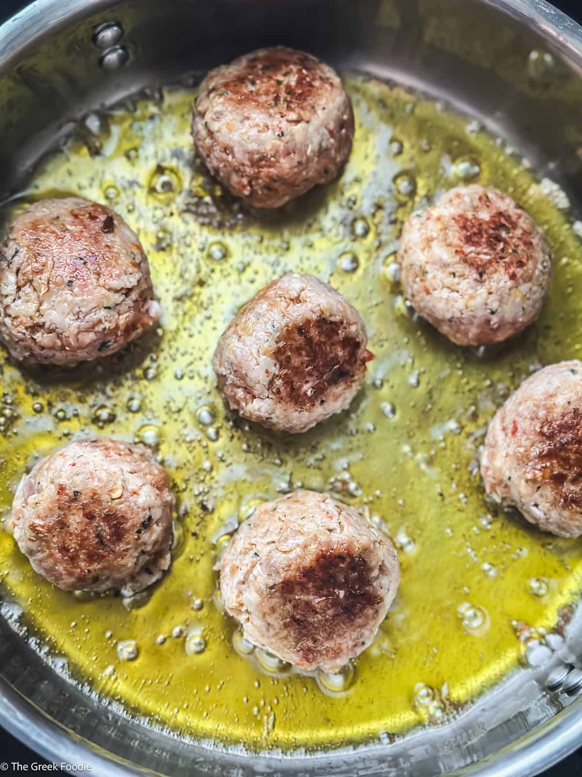 Turkey meatballs browning in olive oil in a skillet before being added to the gravy.