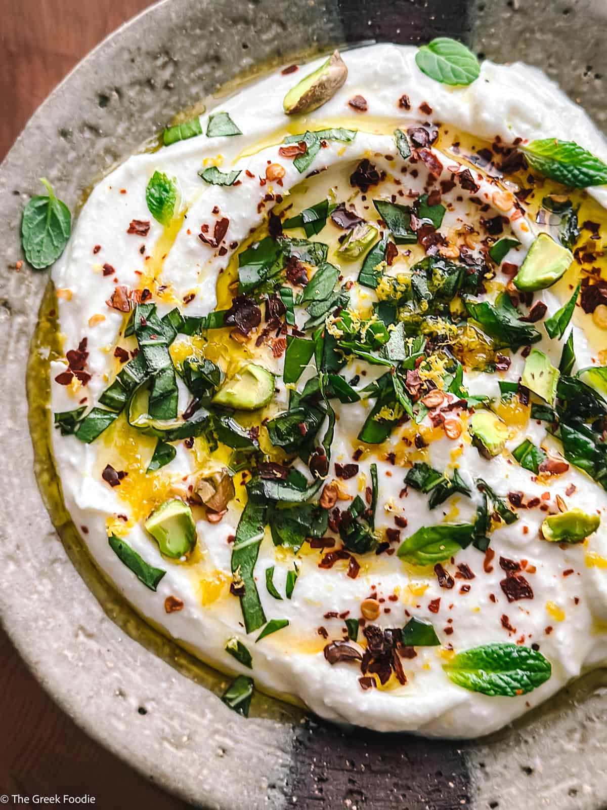 Greek yogurt and feta dip in a ceramic bowl drizzled with olive oil and topped with herbs and chili flakes.