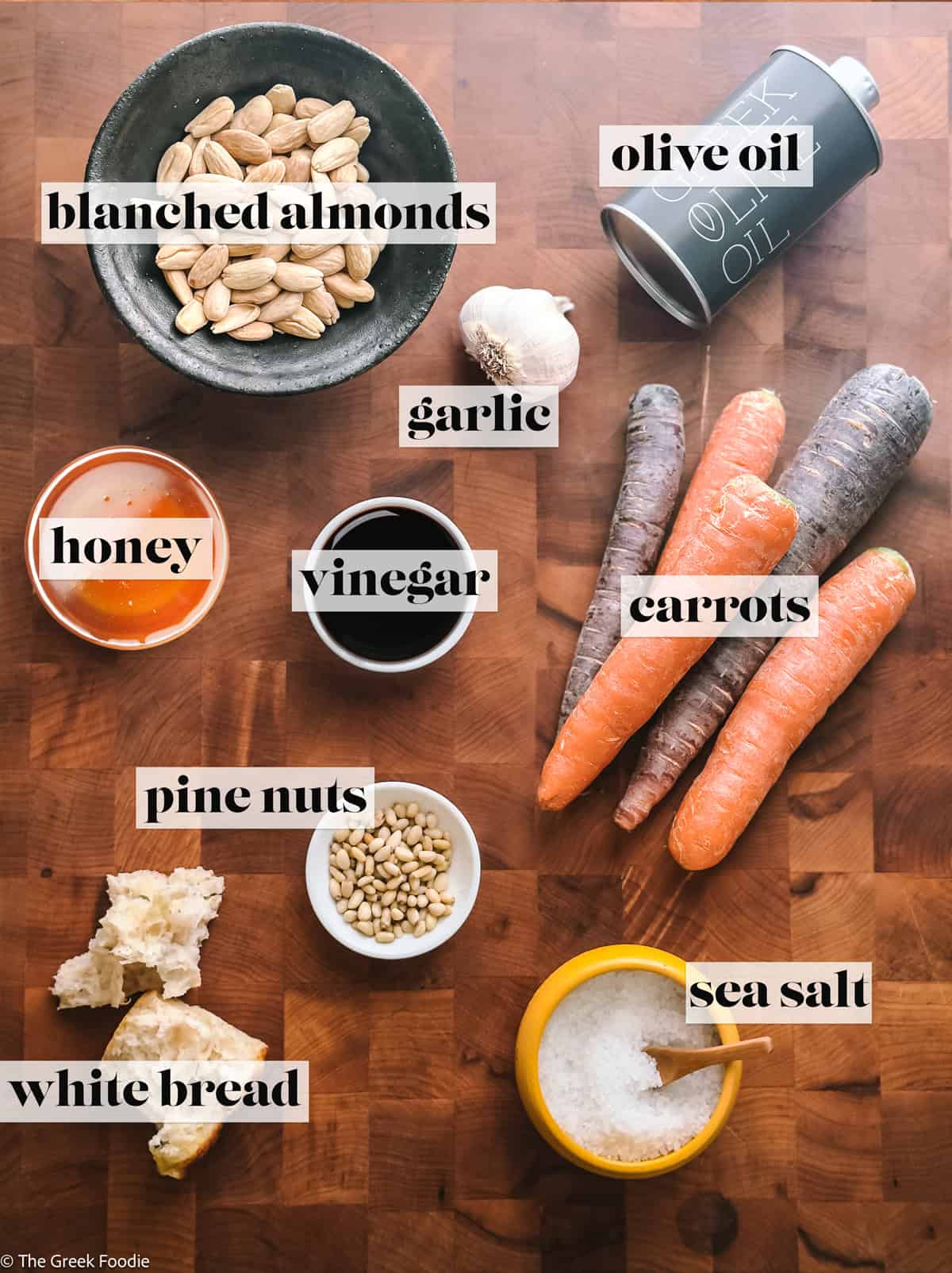 Ingredients for carrot ribbon salad with almond skordalia — heirloom carrots, blanched almonds, roasted garlic, olive oil, vinegar, honey, bread, and pine nuts on a wooden board.