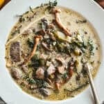 Greek mushroom magiritsa soup in a white bowl with red Easter egg and lemon