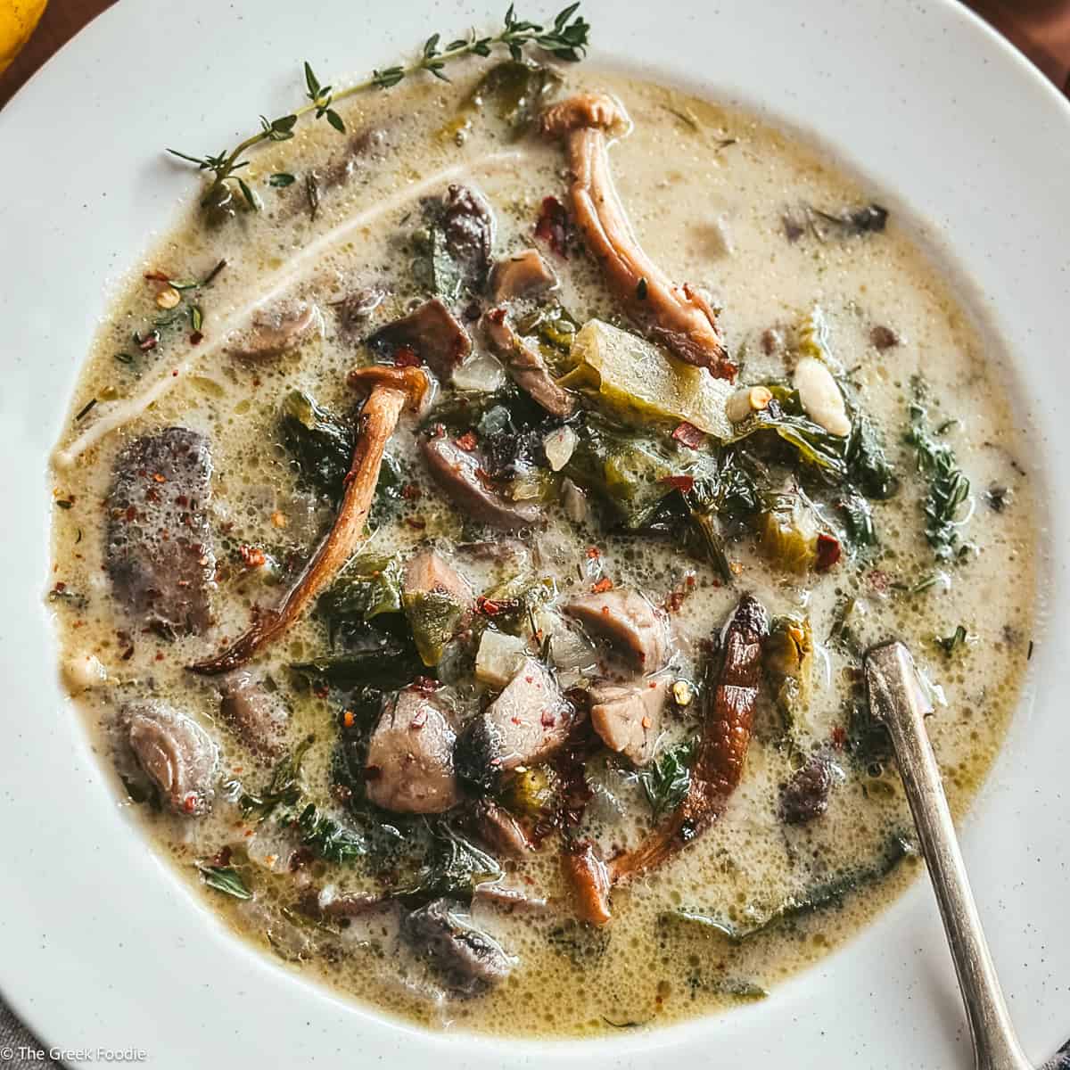 Greek mushroom magiritsa soup in a white bowl with red Easter egg and lemon