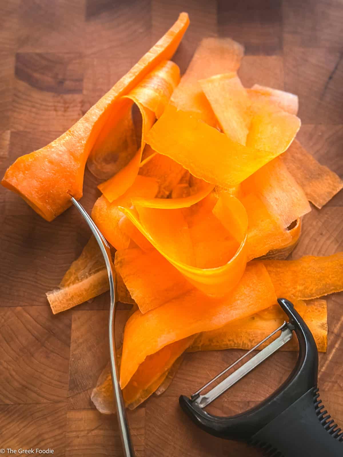 Carrot ribbons shaved with a vegetable peeler on a wooden cutting board.