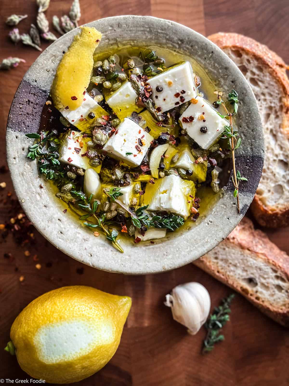 Marinated feta served in a bowl with bread, and fresh herbs
