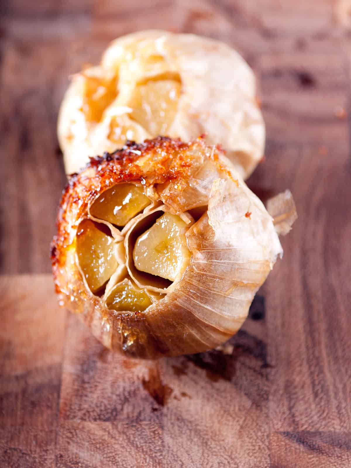A whole head of roasted garlic, golden and caramelized, on a wooden cutting board.
