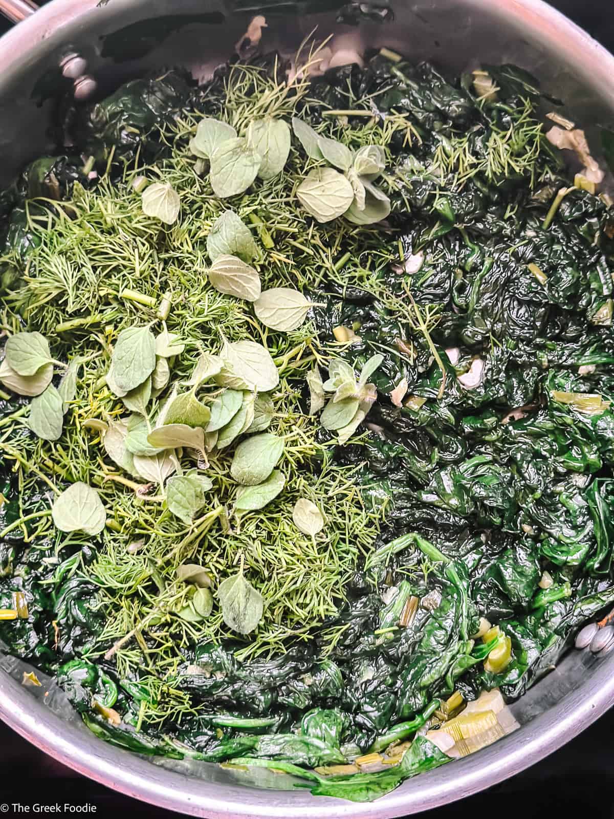Fresh spinach wilting in a pan with dill and oregano for spanakopita tortilla wrap filling