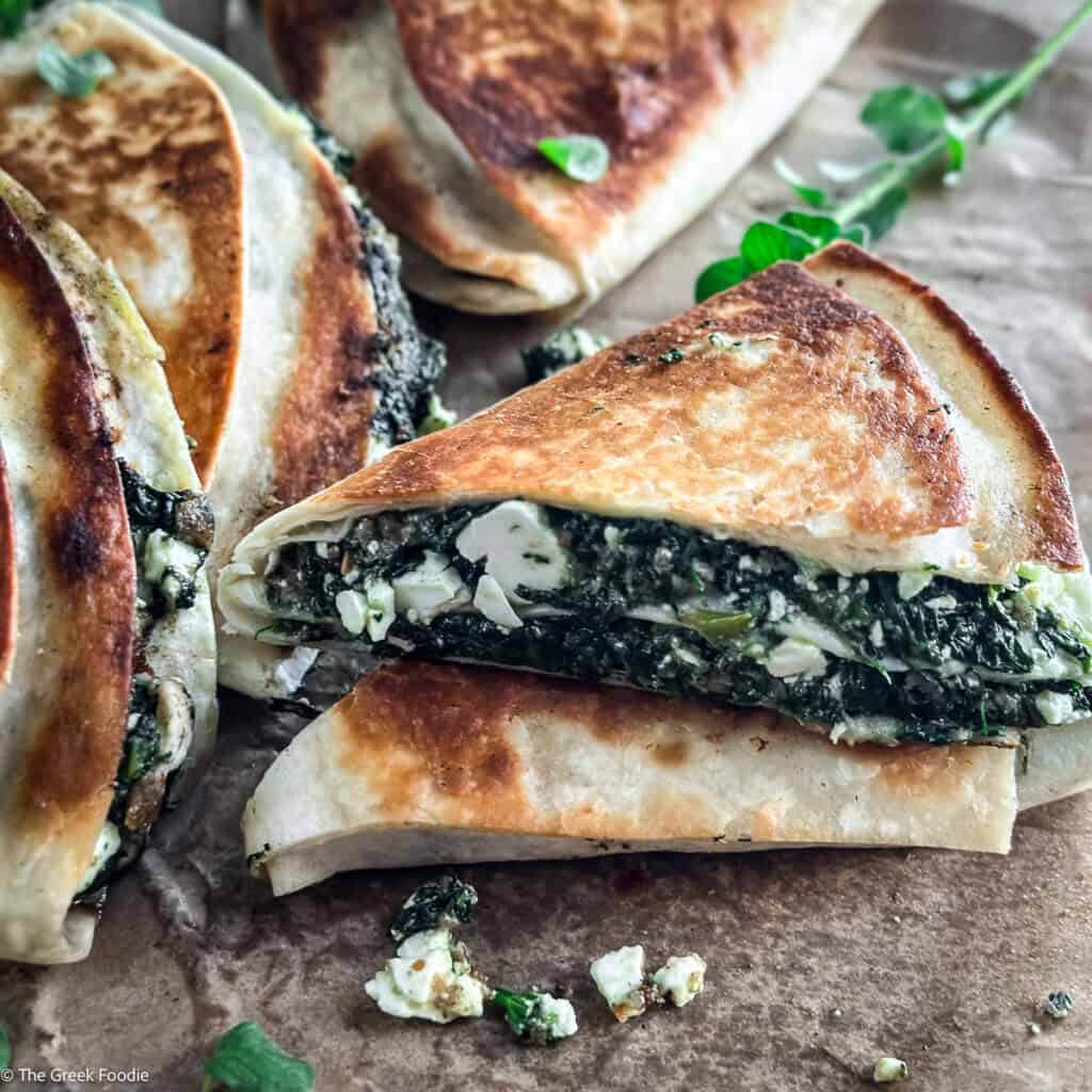 Stack of crispy spinach and feta tortilla wraps spanakopita style with fresh oregano on parchment paper.