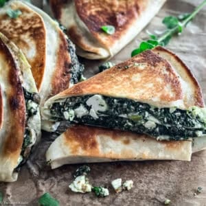 Stack of crispy spinach and feta tortilla wraps spanakopita style with fresh oregano on parchment paper.