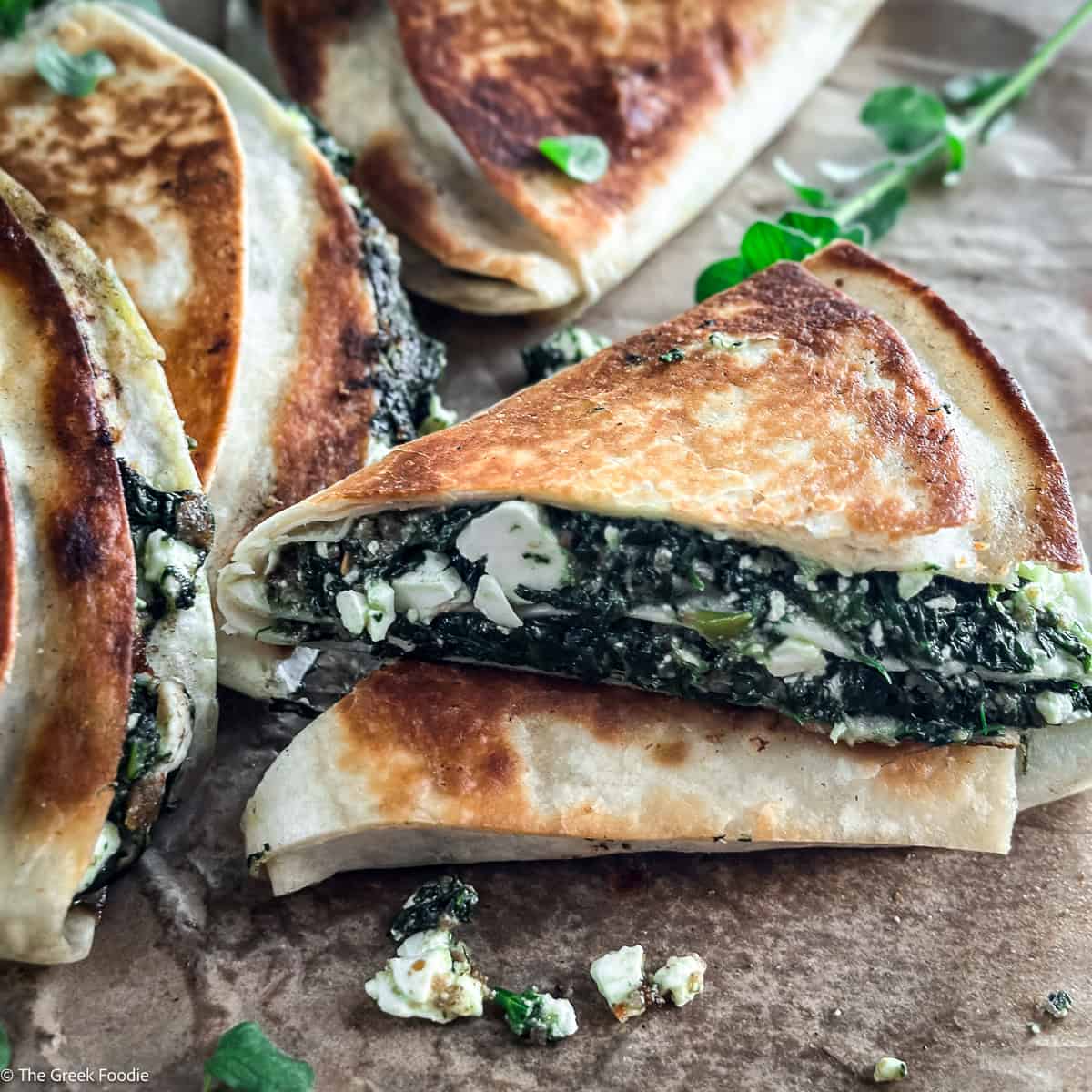 Stack of crispy spinach and feta tortilla wraps spanakopita style with fresh oregano on parchment paper.