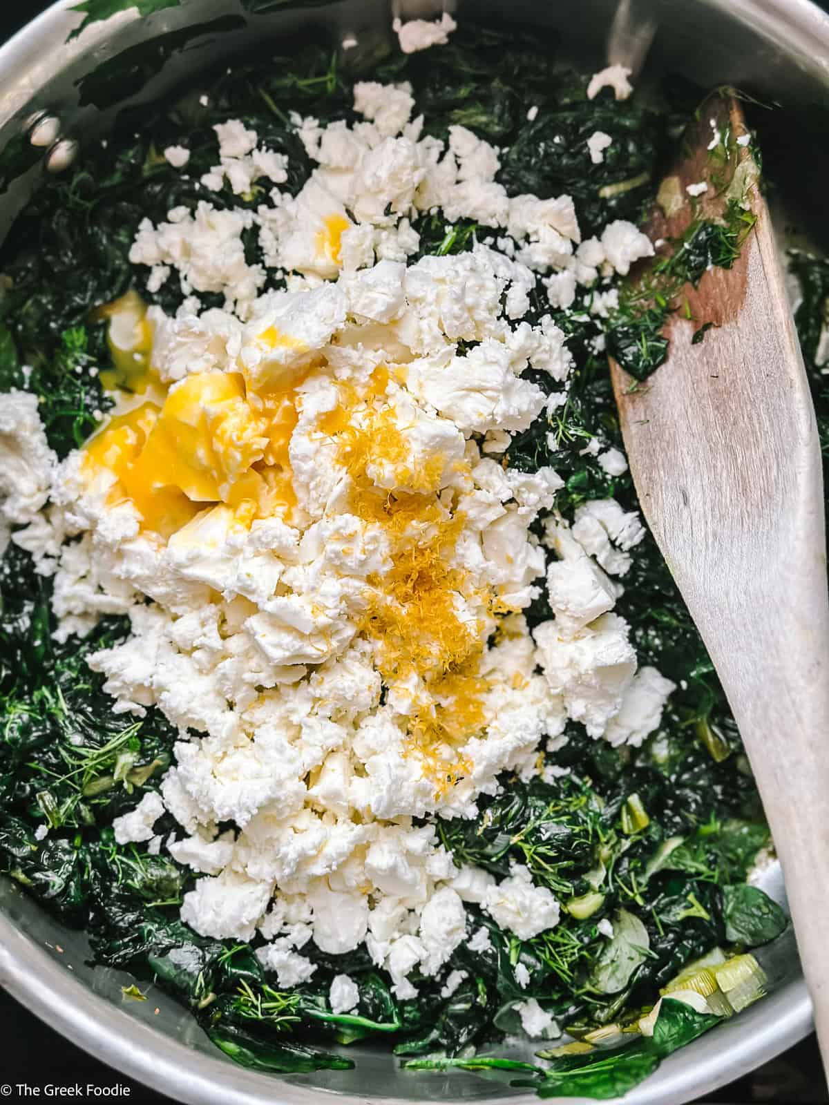 Crumbled Greek feta cheese and egg yolk added to cooled spinach filling for spanakopita tortilla wraps, with lemon zest