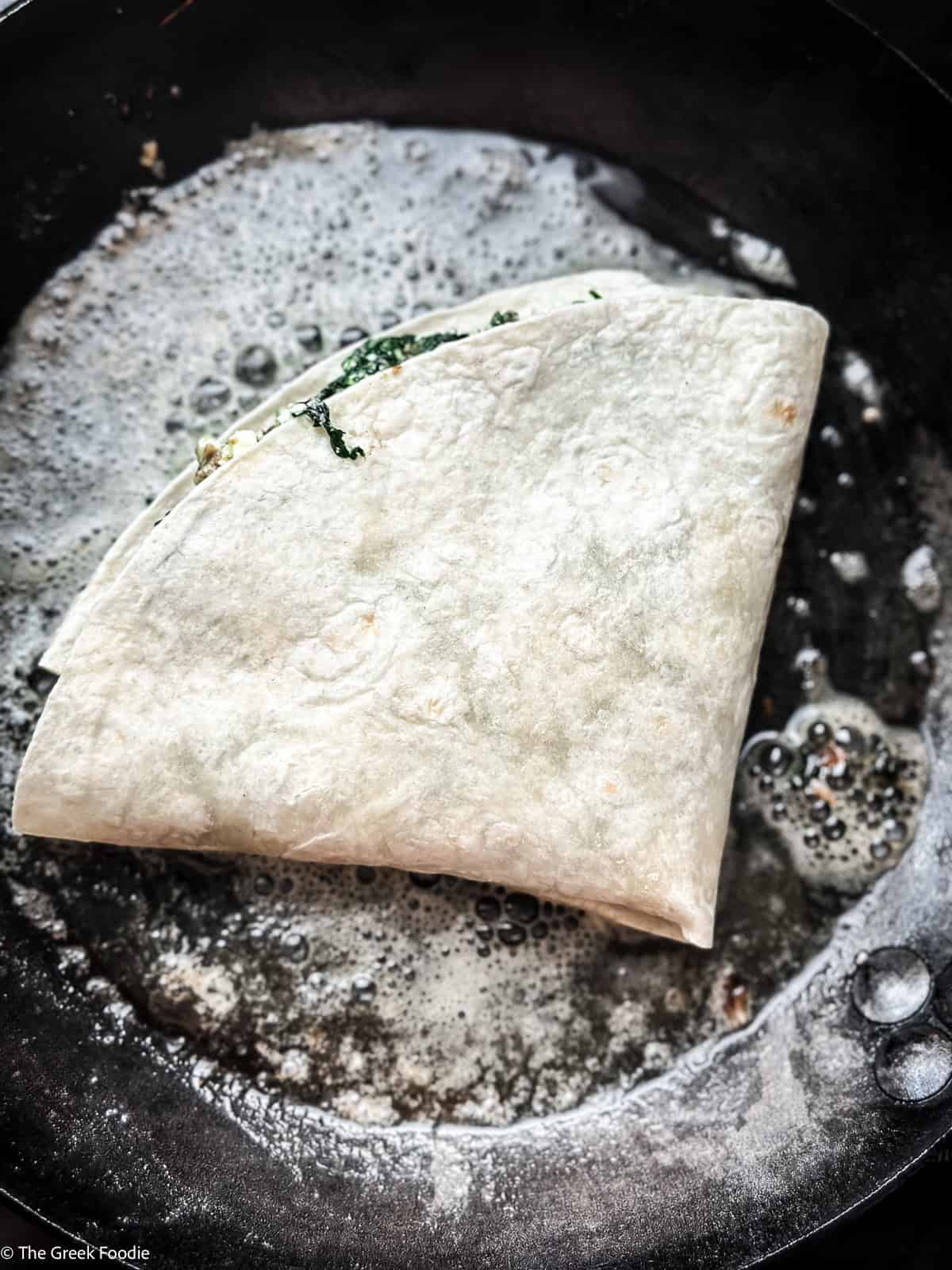 Folded spinach feta tortilla wrap placed seam side down in a buttered cast iron skillet