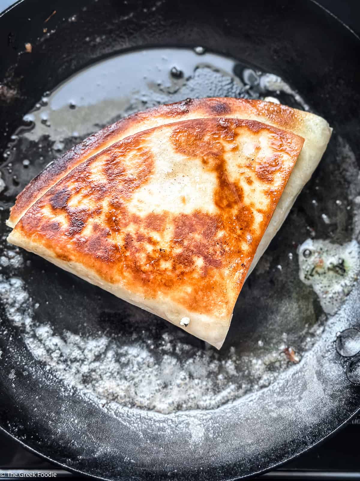 Spanakopita tortilla wrap toasting in a cast iron pan until golden brown and crispy