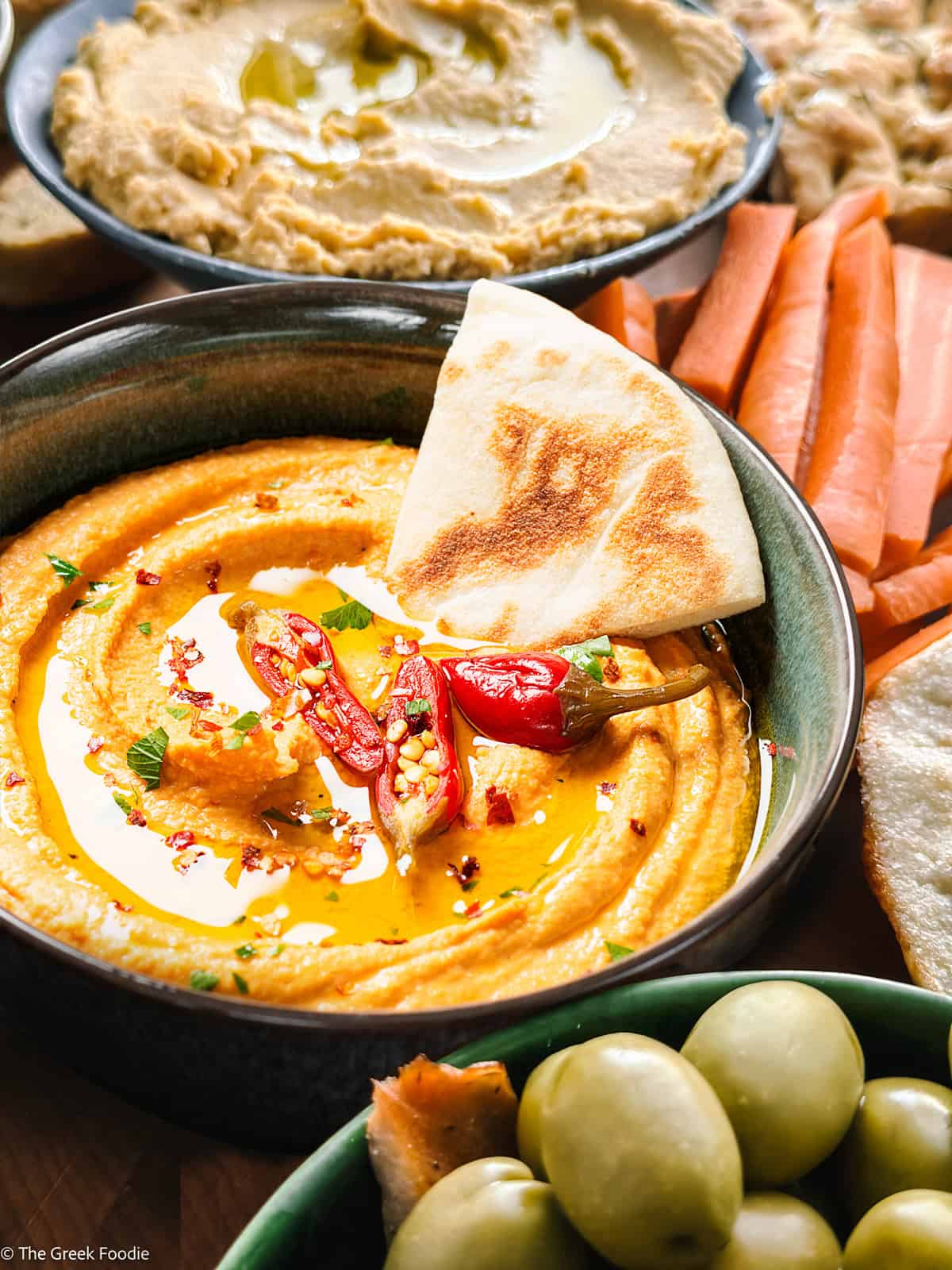 Spicy whipped feta dip served in a bowl with a drizzle of olive oil, chilies on top, and crusty bread on the side.