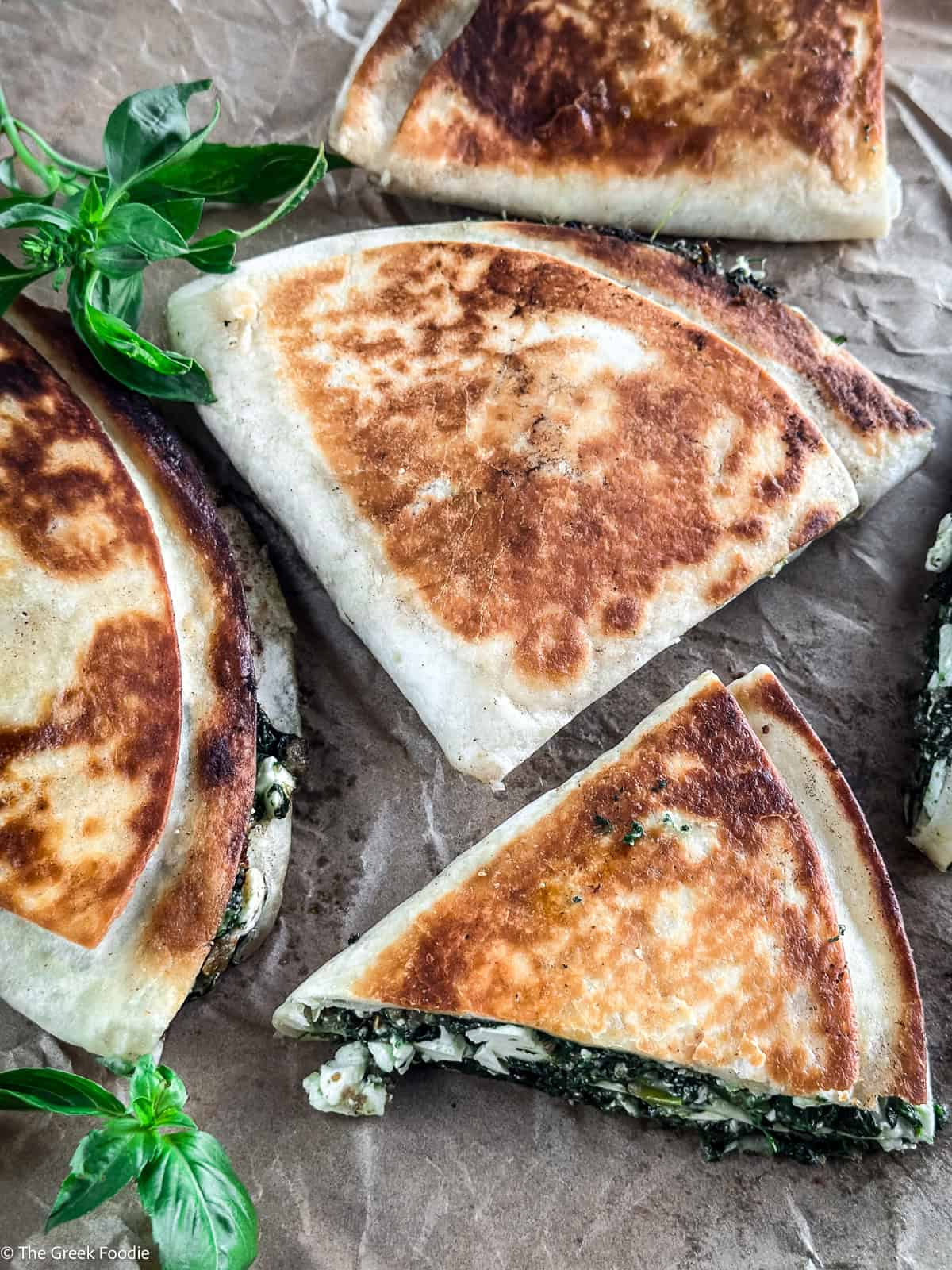 Spanakopita tortilla wraps cut open showing spinach and feta filling, served on parchment paper