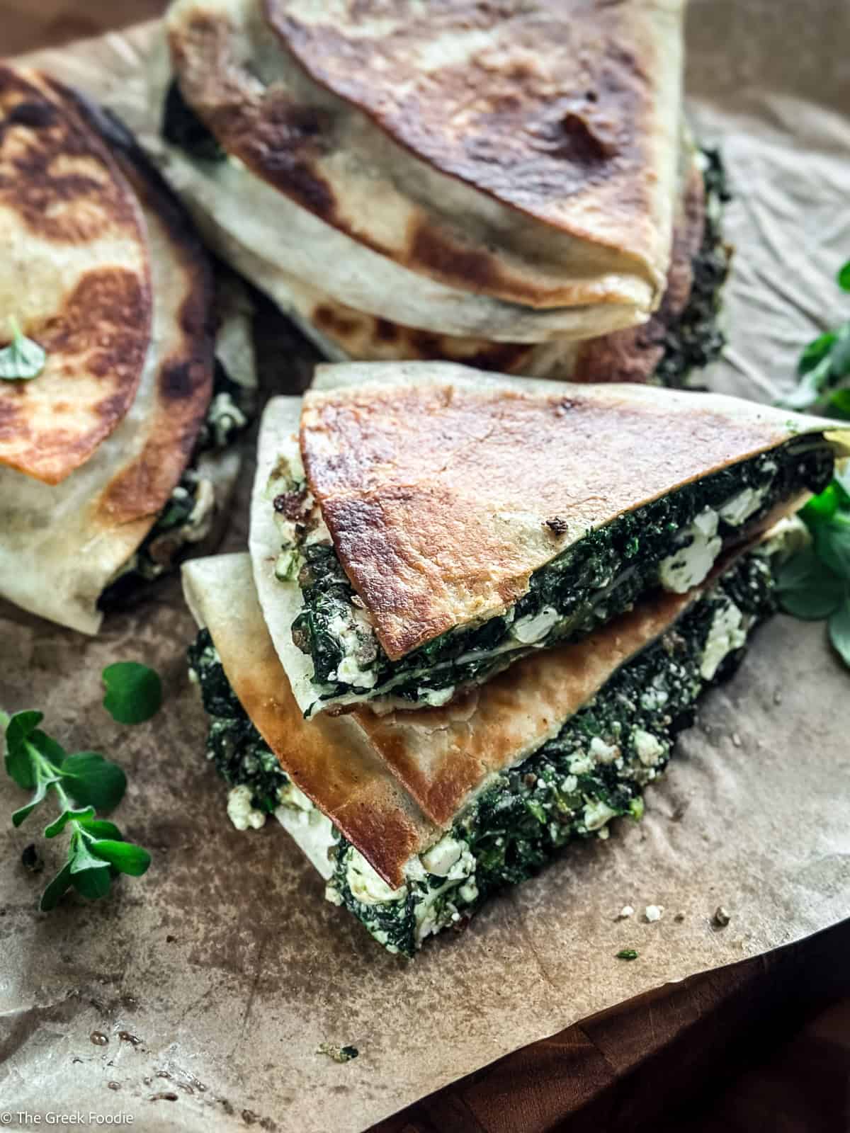 Stack of crispy spinach and feta tortilla wraps spanakopita style with fresh oregano on parchment paper.