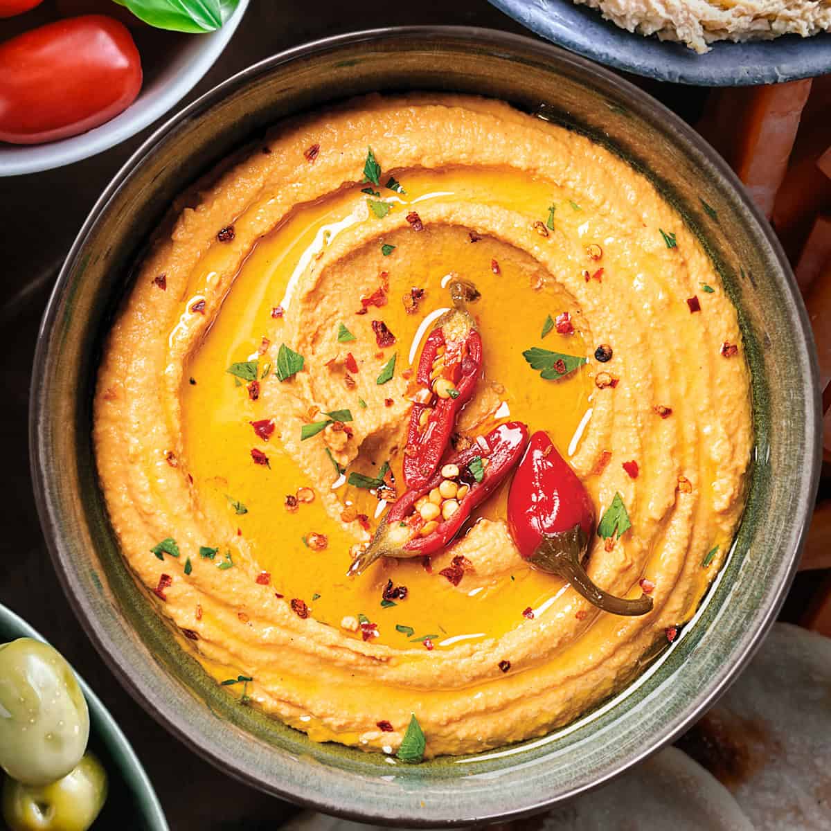 Whipped feta dip (tirokafteri) in a bowl topped with chilies, served with vegetables bead and olives.