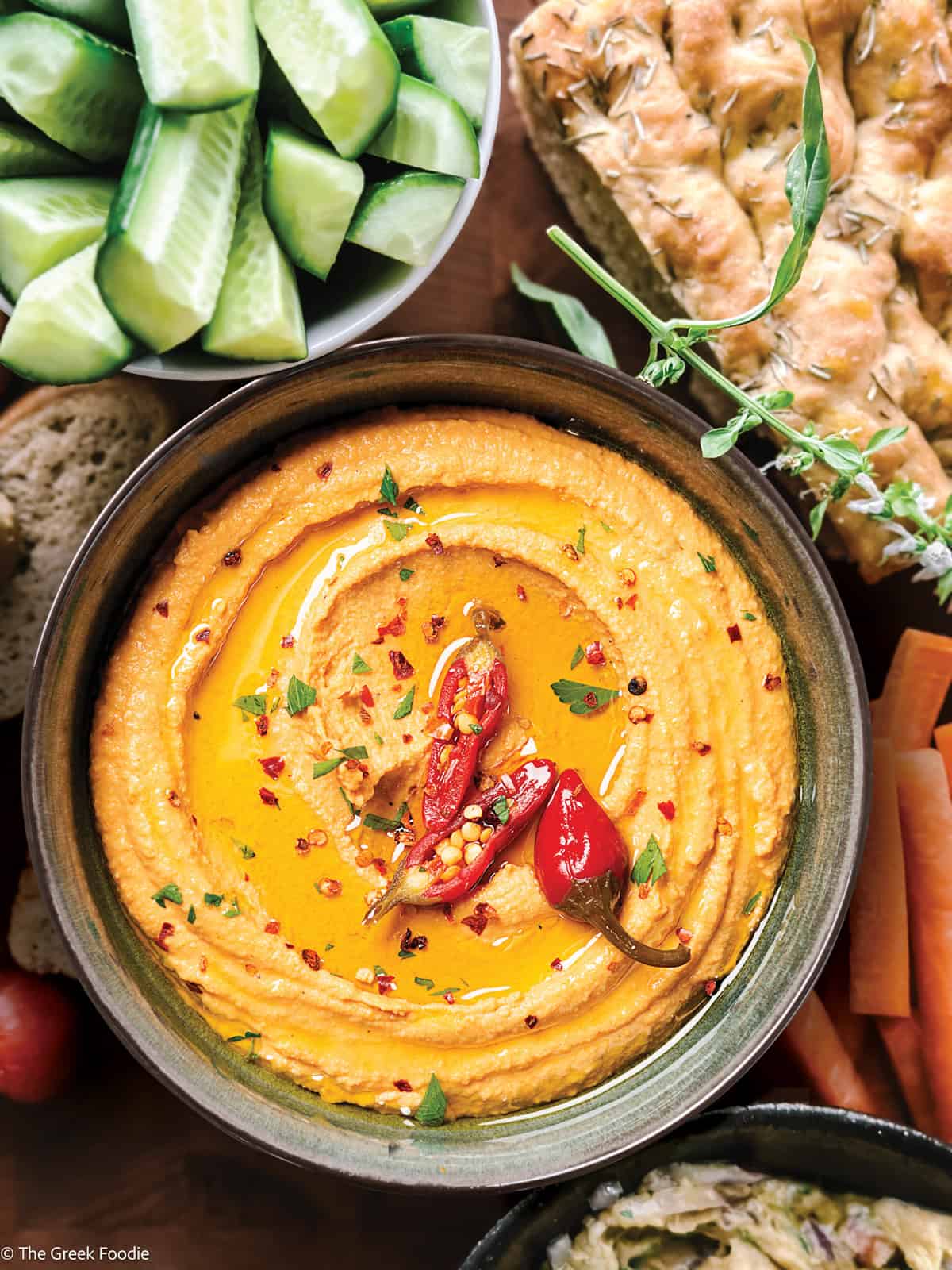 Whipped feta dip (tirokafteri) in a bowl topped with chilies, served with vegetables bead and olives.