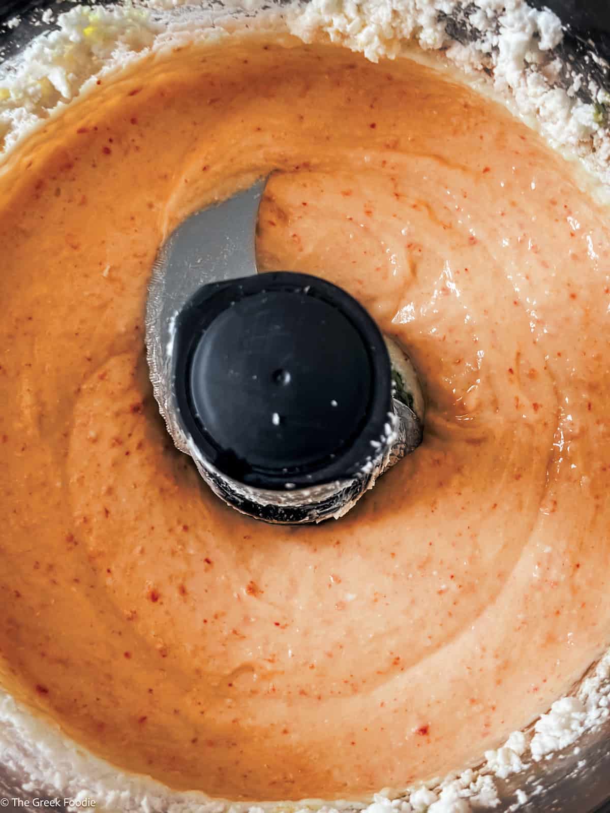 Creamy whipped feta dip in a food processor after blending with yogurt and peppers.